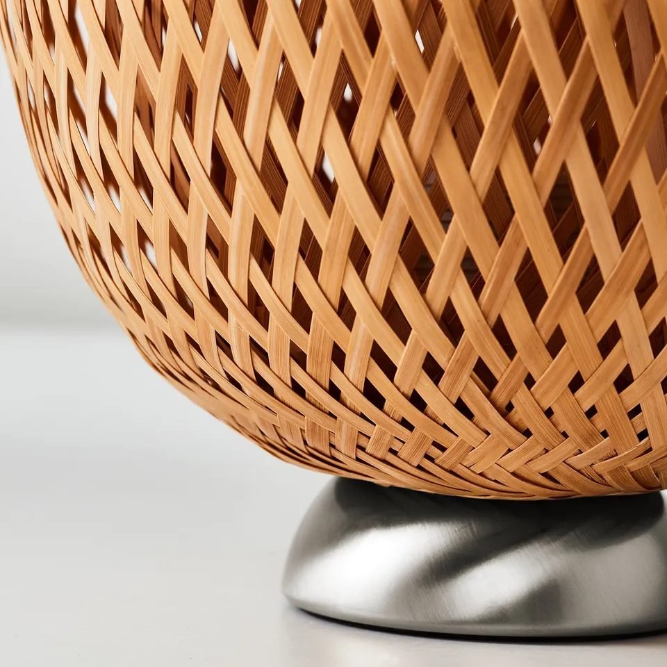 Woven bamboo shade lamp with metallic base, showcasing intricate craftsmanship.
