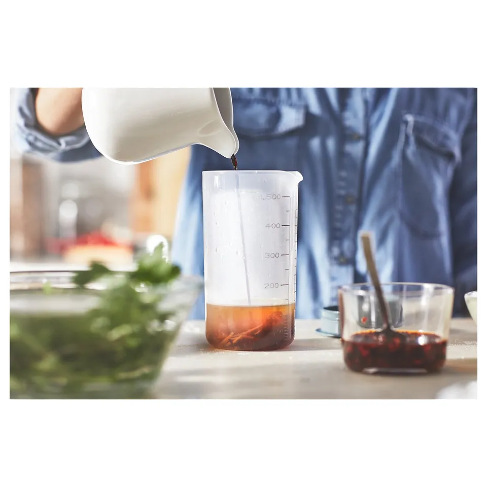 Person pours liquid into a clear, white, and brown graduated measuring cup, surrounded by other kitchen items.