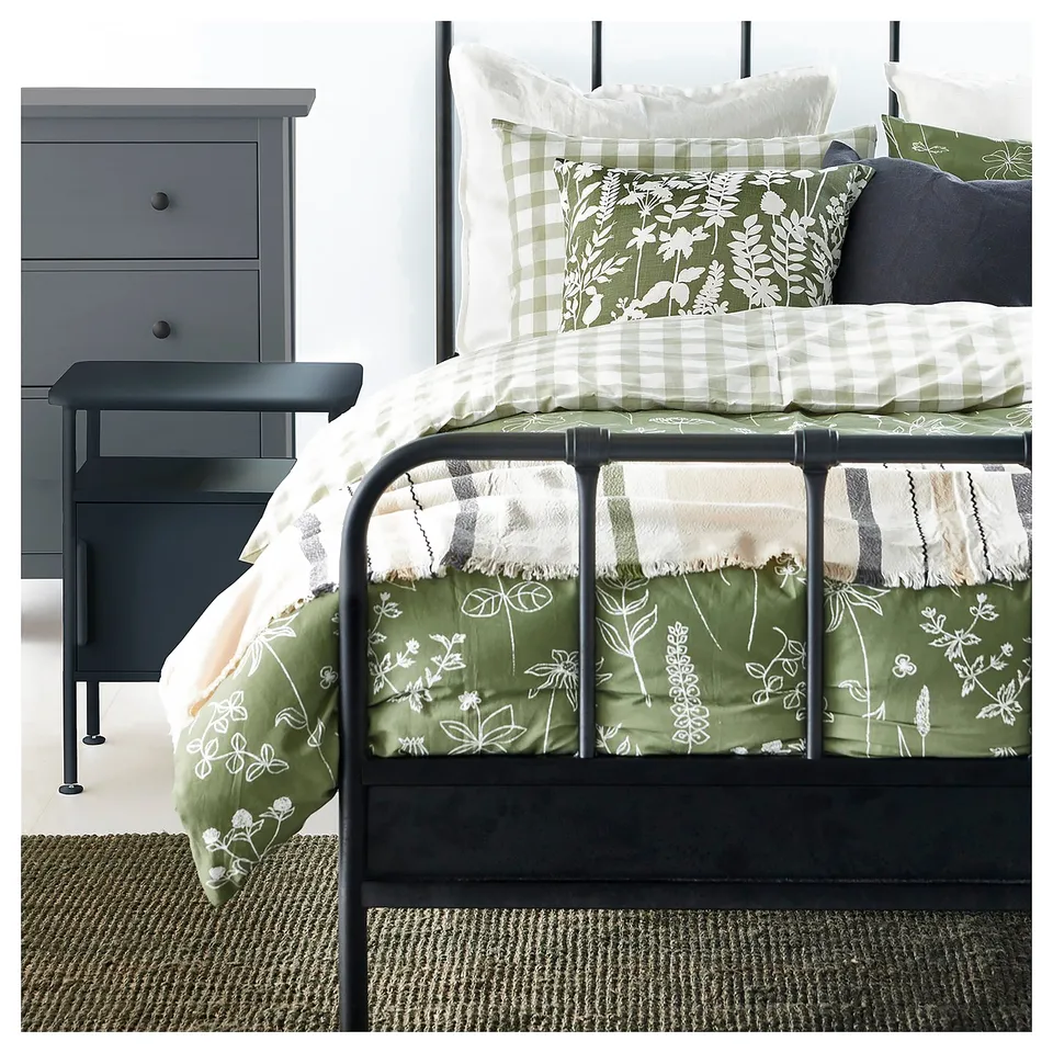 Cosy bedroom with black metal bed, green floral bedding, grey bedside table, and textured rug.