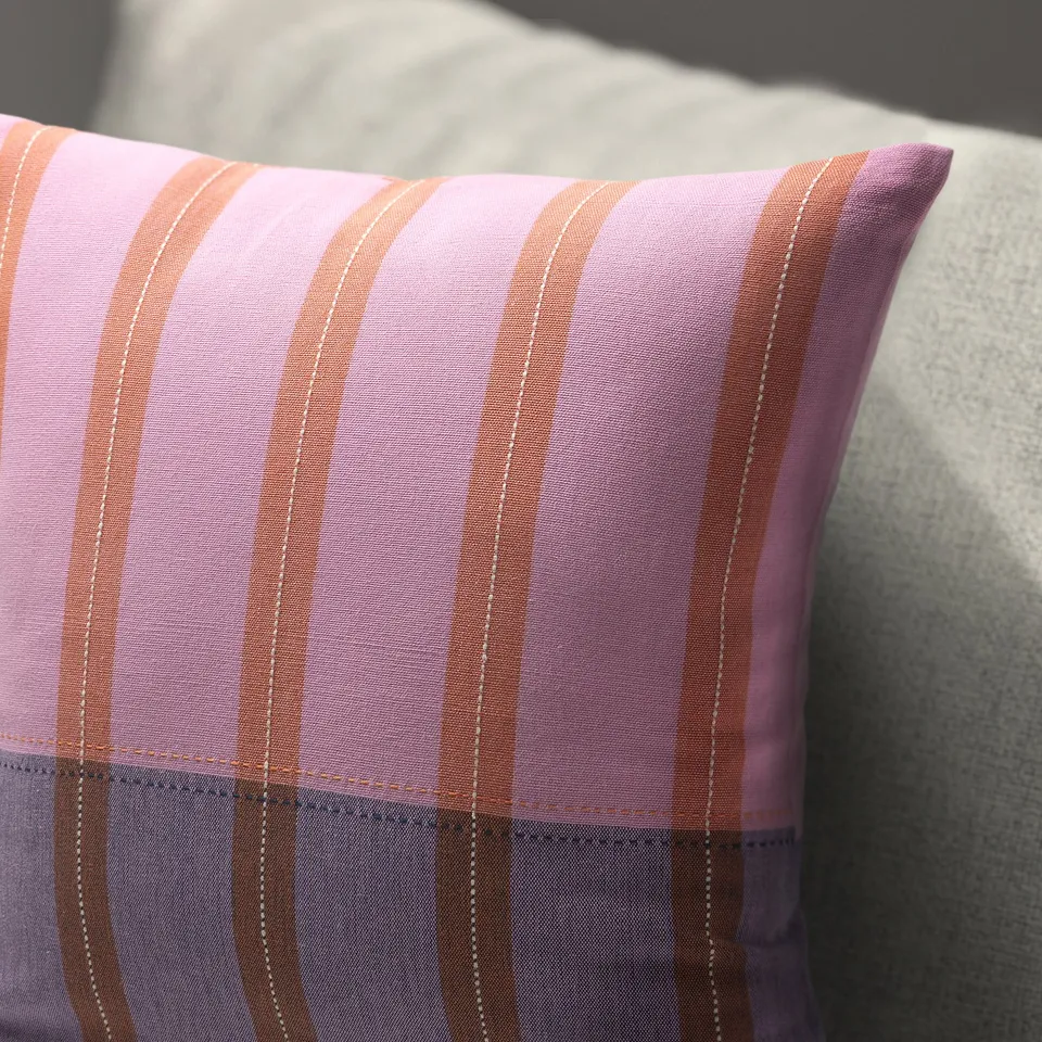 A close-up of a handwoven, striped purple and orange cushion cover, showcasing its soft cotton texture and precise stitching.