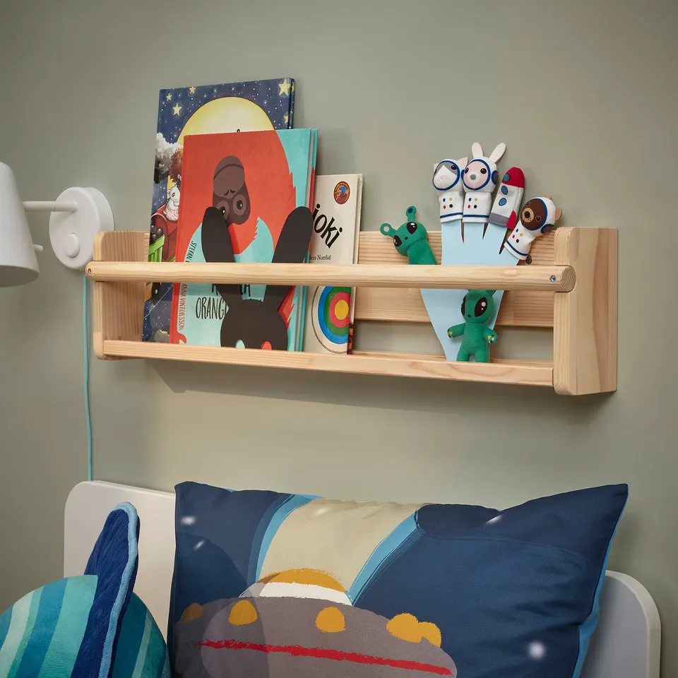 Wooden shelf with kids books & toys above blue bed.