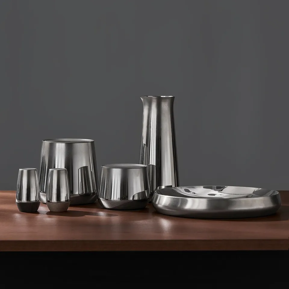 Stainless steel kitchen set on table: pitcher, cups, bowl, and containers. Modern, elegant design for serving and storage.