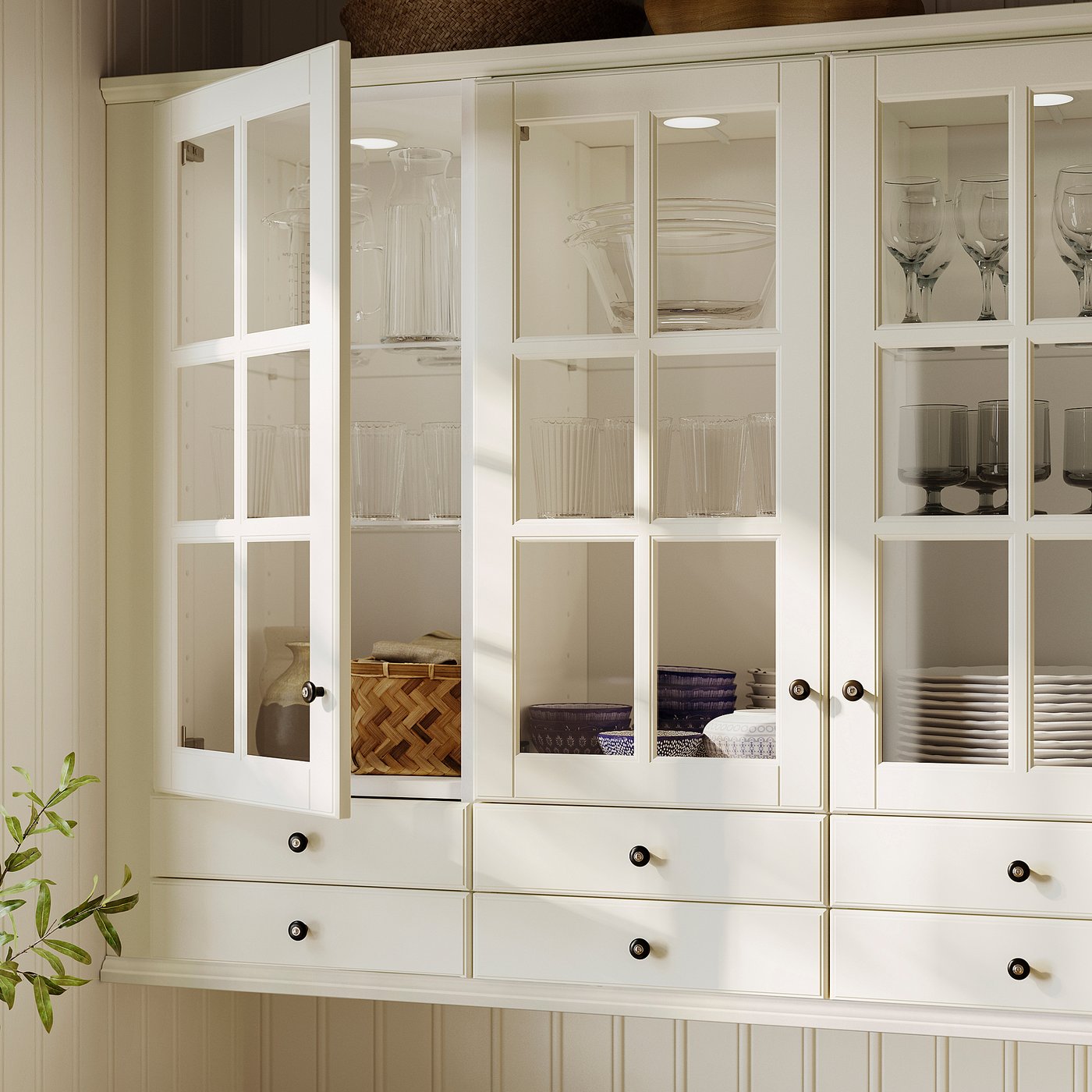 White kitchen cabinet with glass doors, showing dishes and glasses, off-white colour, panelled design, wooden and glass material.