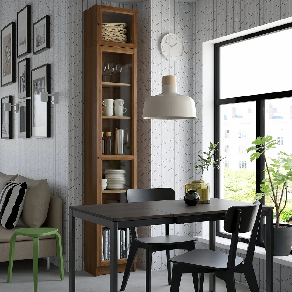 Modern dining room with black table, chairs, window, stool, plant, clock, lamp, bookcase, photos, couch.
