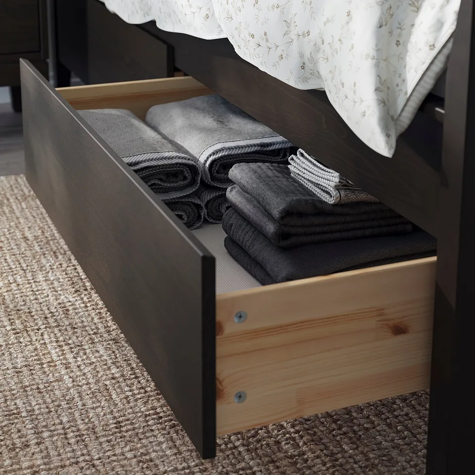 Dark wooden bed with open drawer showing folded grey blankets.
