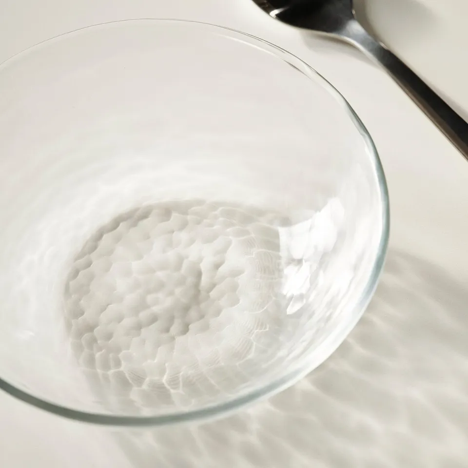 Glass bowl with ribbed texture on white surface, shadows cast, spoon beside it.