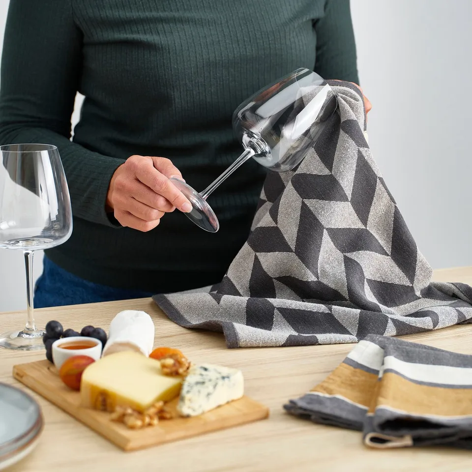 Person pouring wine, surrounded by cheeseboard and towels on table.