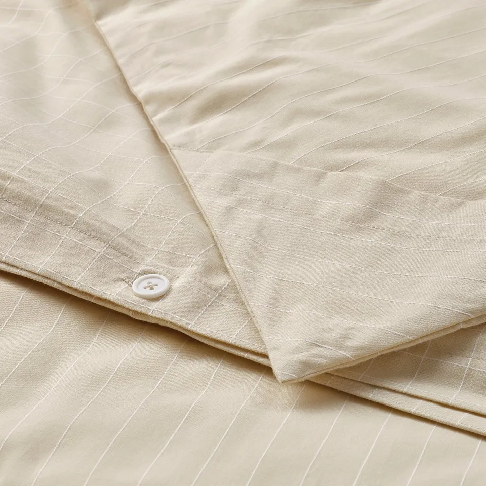 Beige duvet cover with chequered and striped patterns, showing corner button to secure duvet.