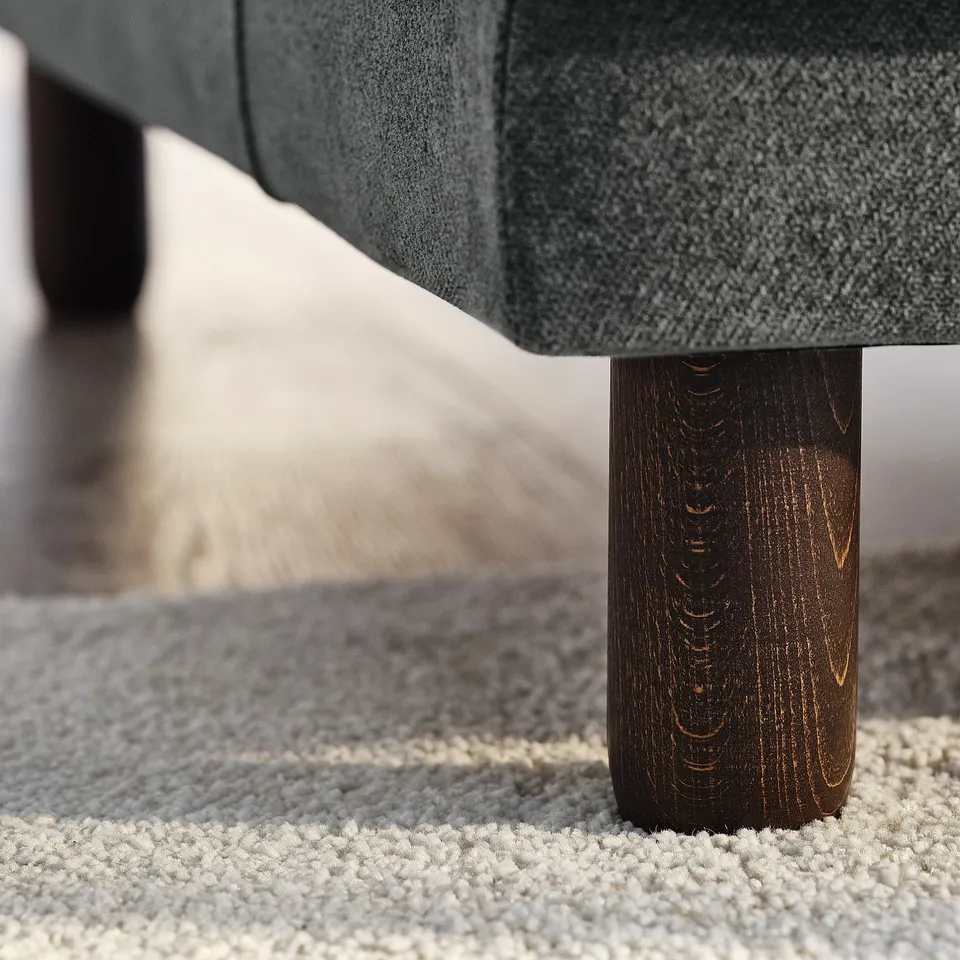 Modern sofa with dark wooden legs, textured grey fabric, positioned on a soft rug.