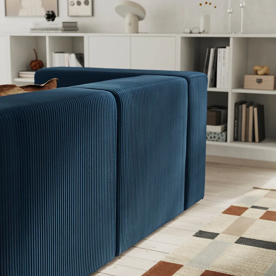 A dark blue corduroy sofa with storage, on a patterned rug, in front of a bookshelf.