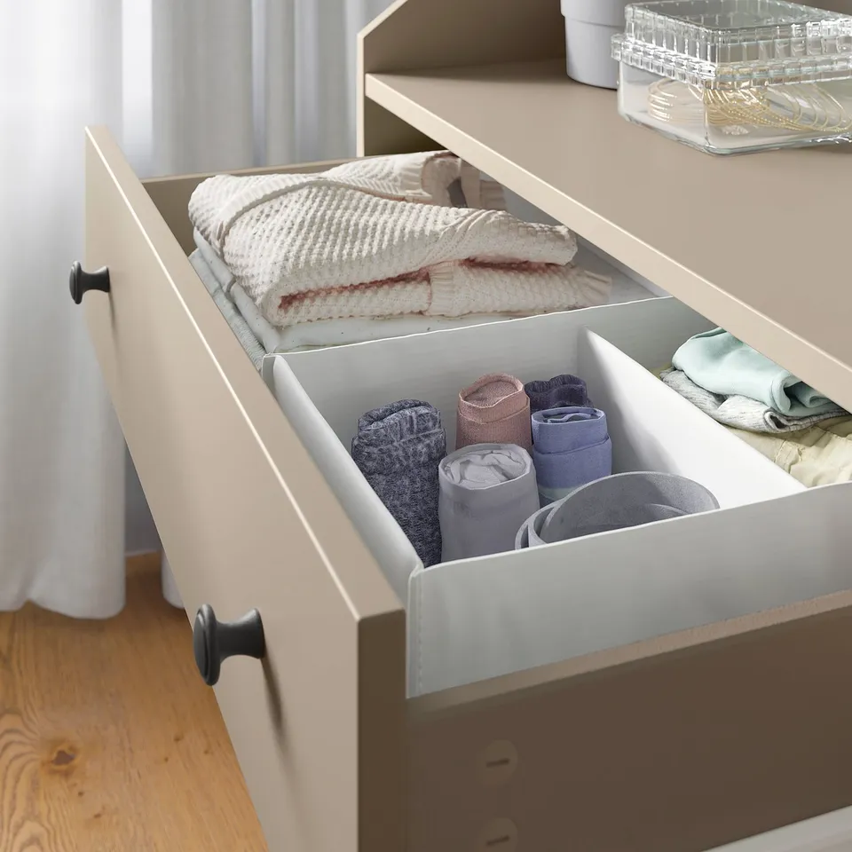 Open white HAUGA chest drawer showing folded clothes and rolled socks.