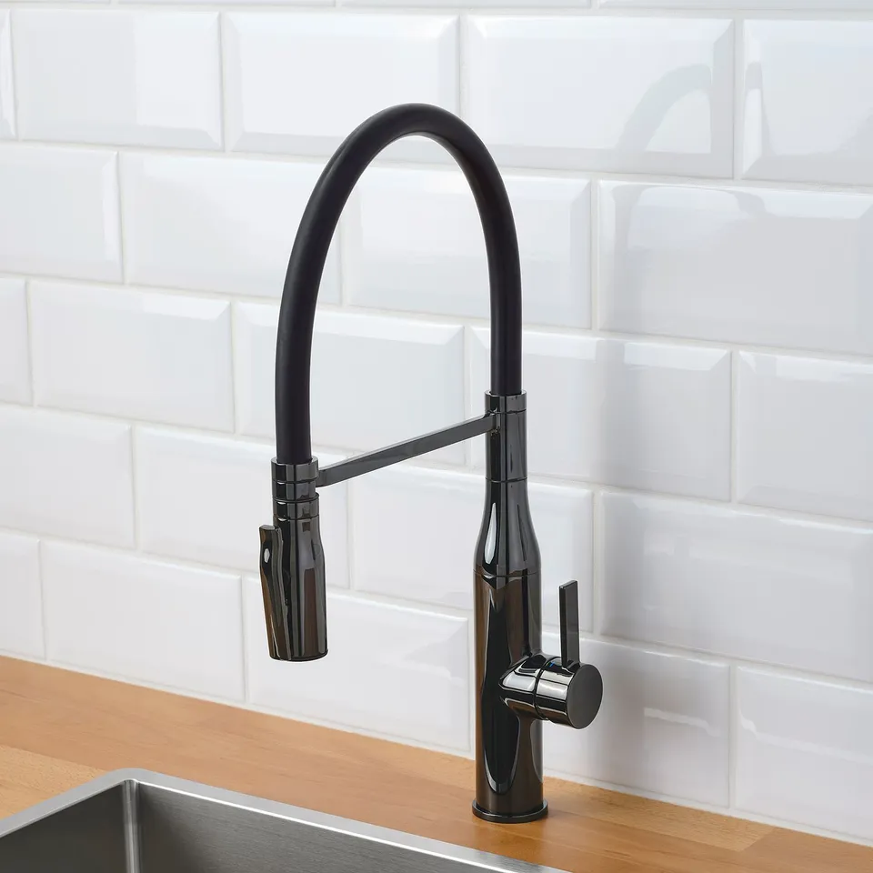 Black kitchen tap with pull-down sprayer, set against white subway tiles, mounted on light wood countertop over stainless steel sink.