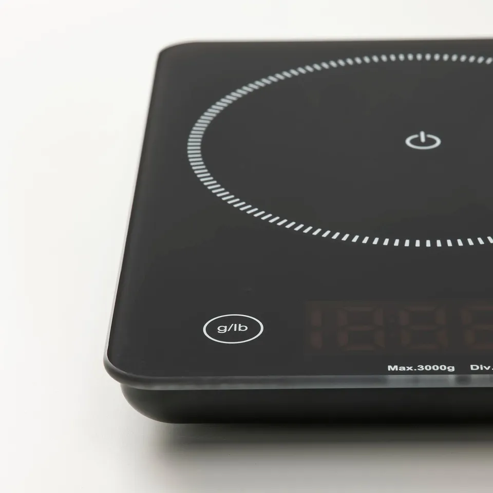 Black digital scale with glass surface, featuring circular light display and power button, resting on a white background.