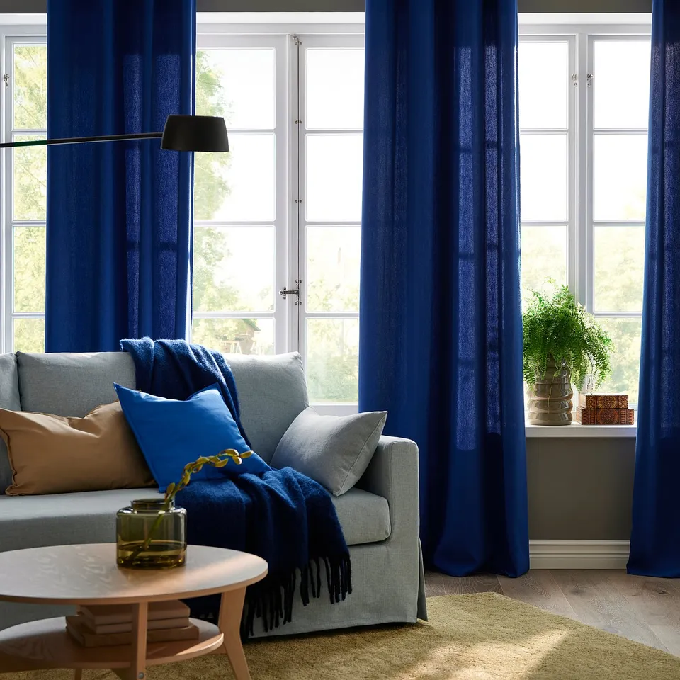 Living room with blue curtains, sofa, and vase.