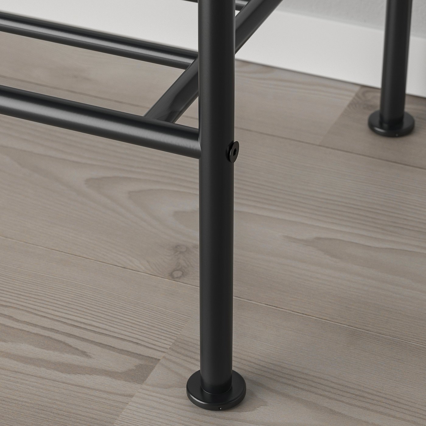 Black metal clothes rack leg with adjustable foot on wooden floor.