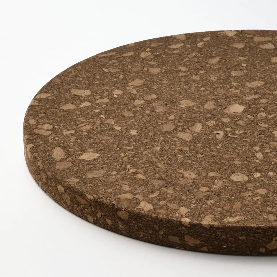 Circular cork trivet on white surface. Dark brown with varied light brown cork specks. Smooth and even texture.