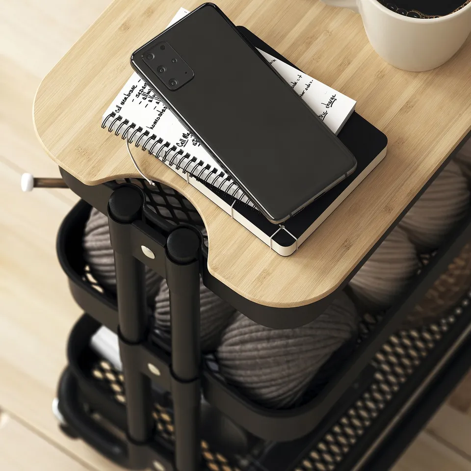 A mobile storage trolley with a wooden top holding a notebook and smartphone, showcasing its portability and additional workspace functionality.