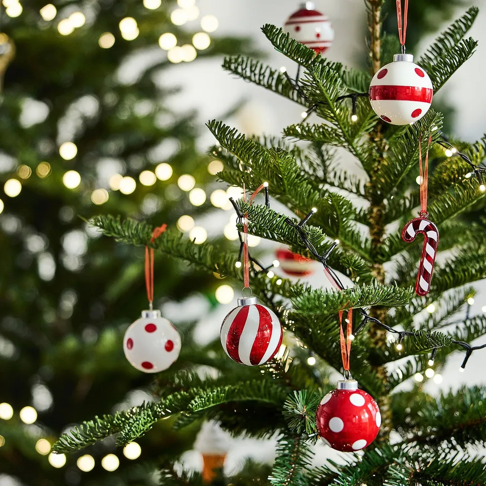 Christmas tree decorated with red and white polka-dot and striped baubles; warm lights in background.