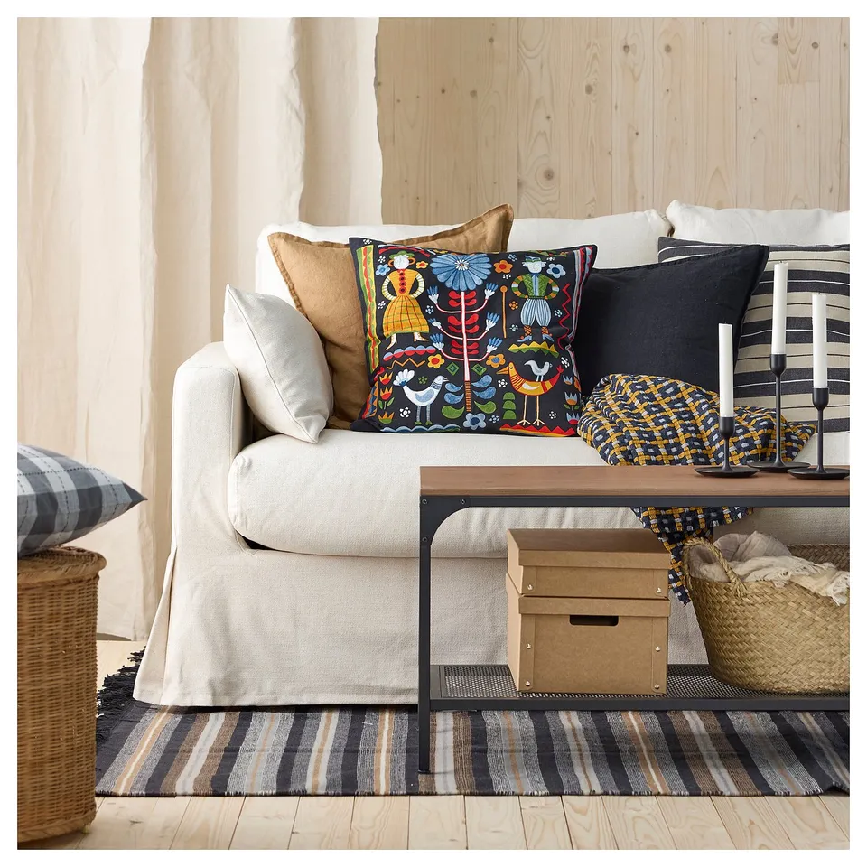 Cosy living room with cream sofa, colourful floral pillow, black and white striped rug & candle holder. Handwoven wool rug on wooden floor.