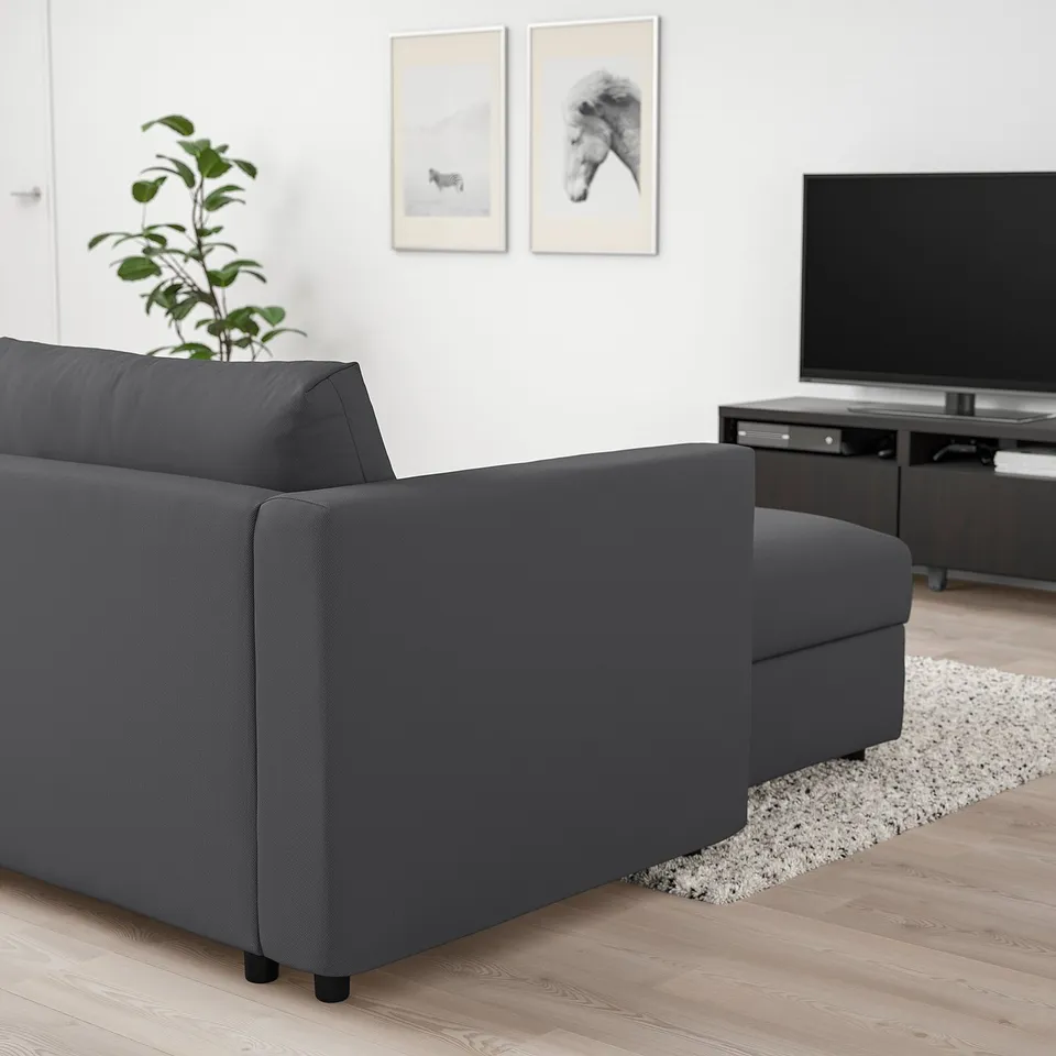 Modern living room with grey VIMLE sectional sofa, wide tv stand, and decorative art. Floor plant and patterned rug complement the minimalist design.