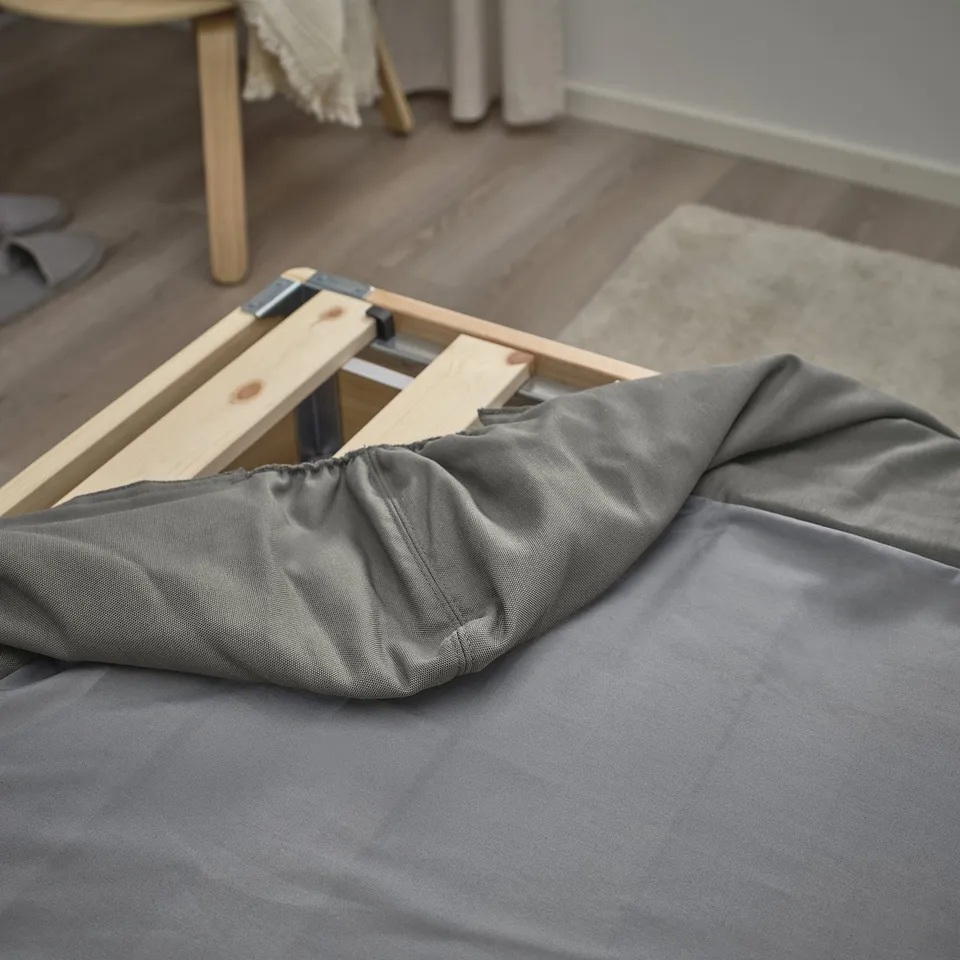 Grey bed sheet with zip on wooden frame, partially removed for cleaning.
