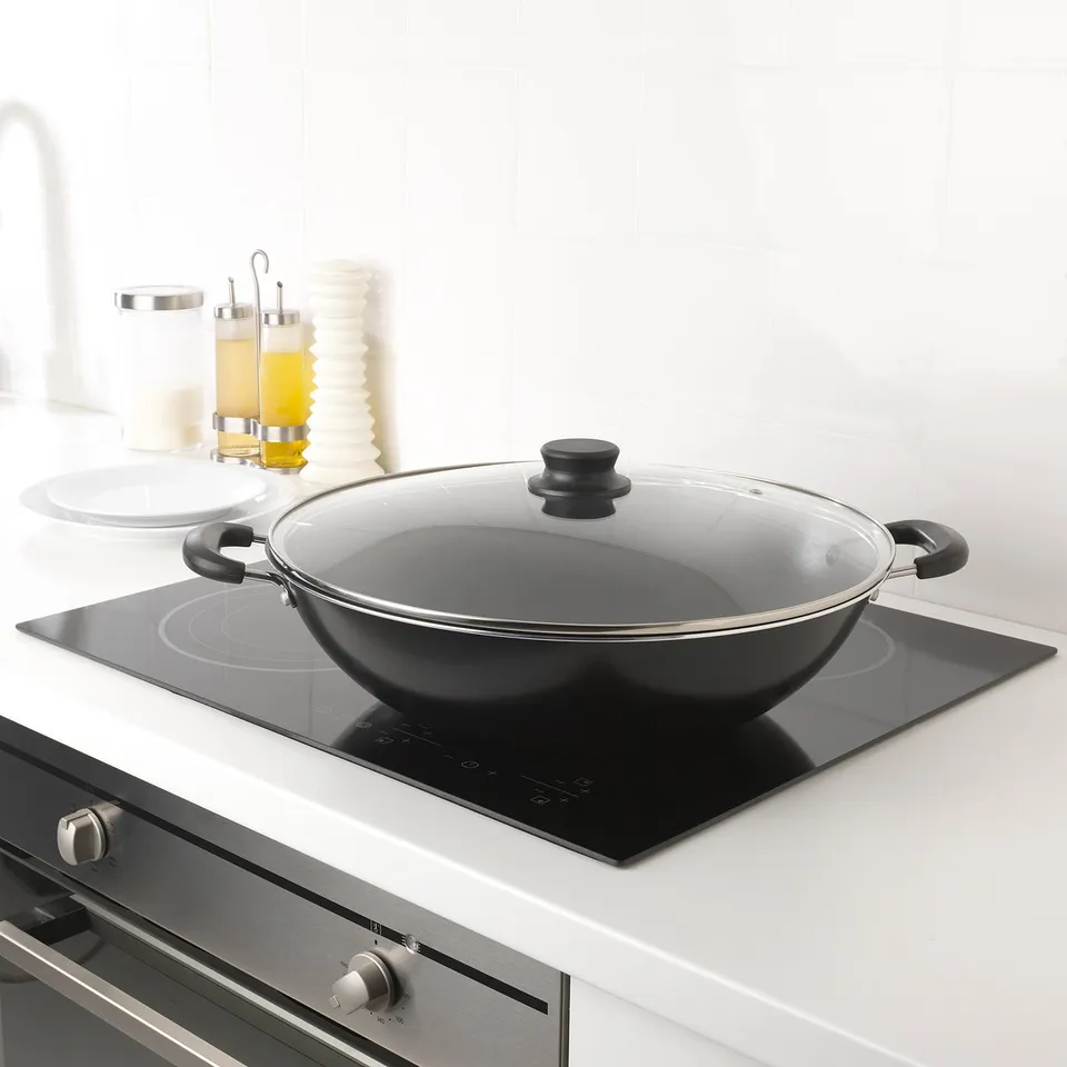 Modern kitchen with black wok on induction hob, two handles, white countertop, cooking tools.