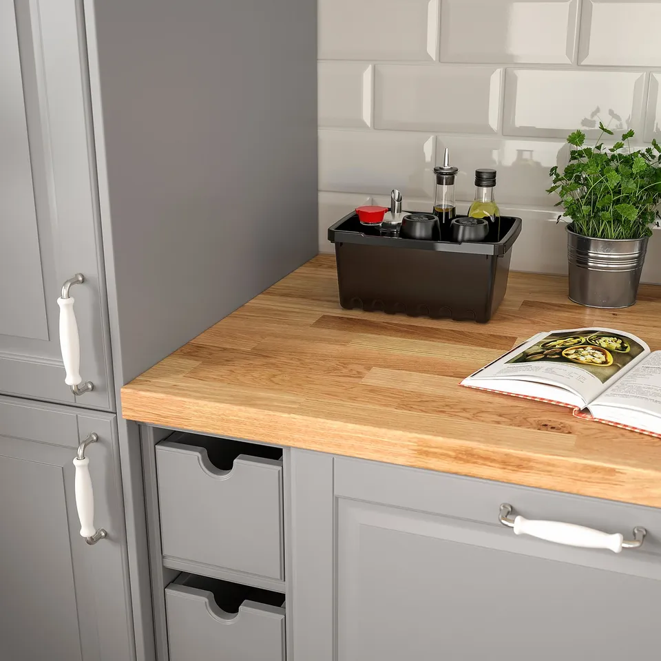 Kitchen counter with light wood countertop, featuring current cooking magazine, small potted herb, and organised spice tray.