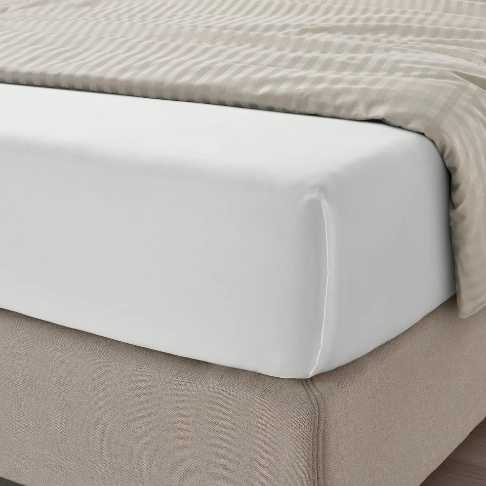 A neatly made bed with white, silky sheets. Sheets are sateen-woven from cotton and lyocell, designed for comfort and easy sleep.