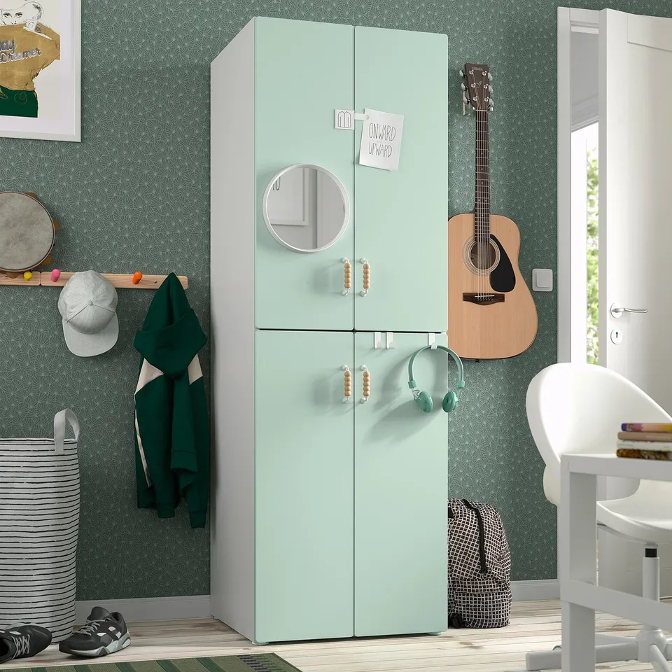 Mint green SMÅSTAD wardrobe with doors, mirror, guitar, coat rack, and chair with books.