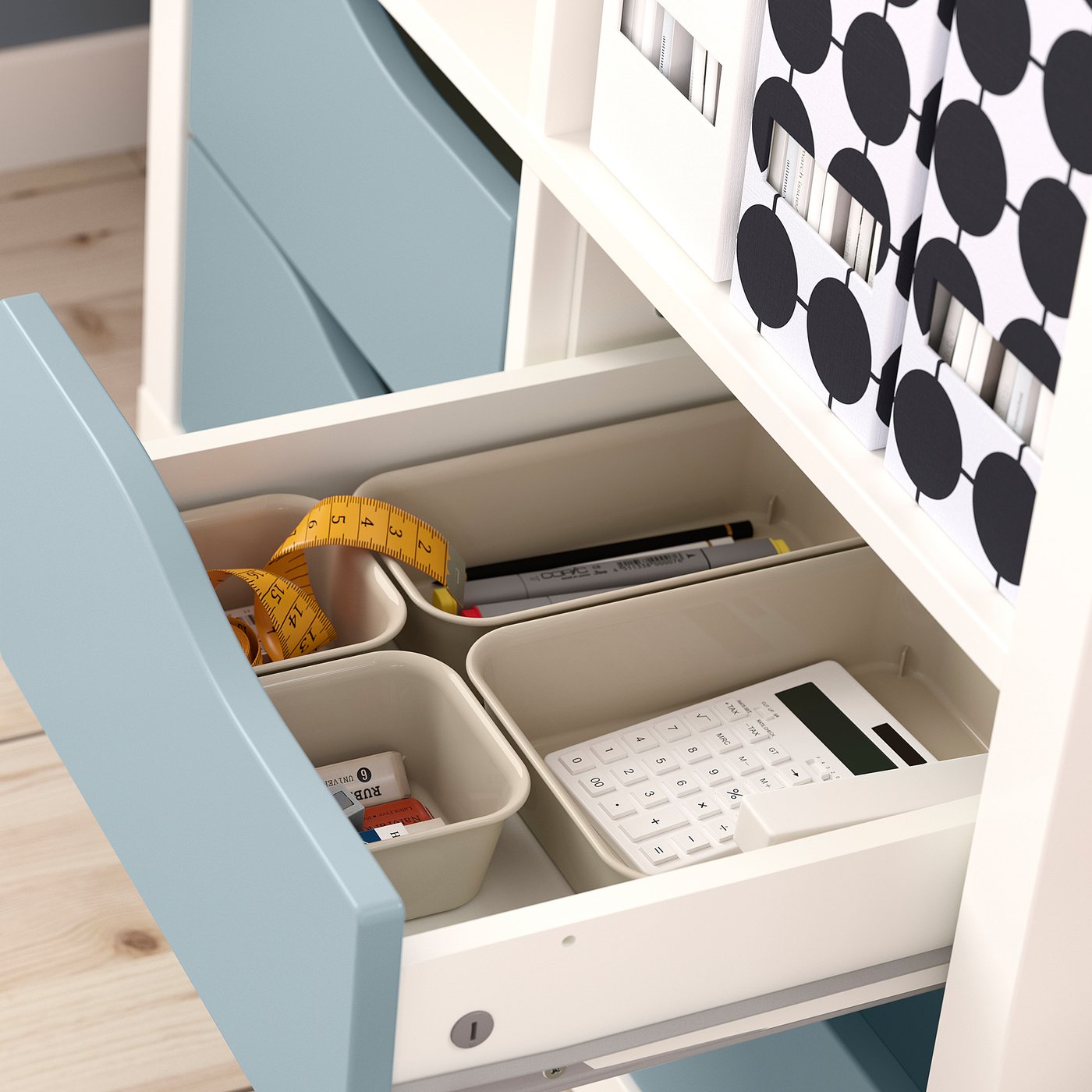 A KALLAX organiser with storage drawers. Drawers hold a tape measure, calculator, pens, and small containers with items.