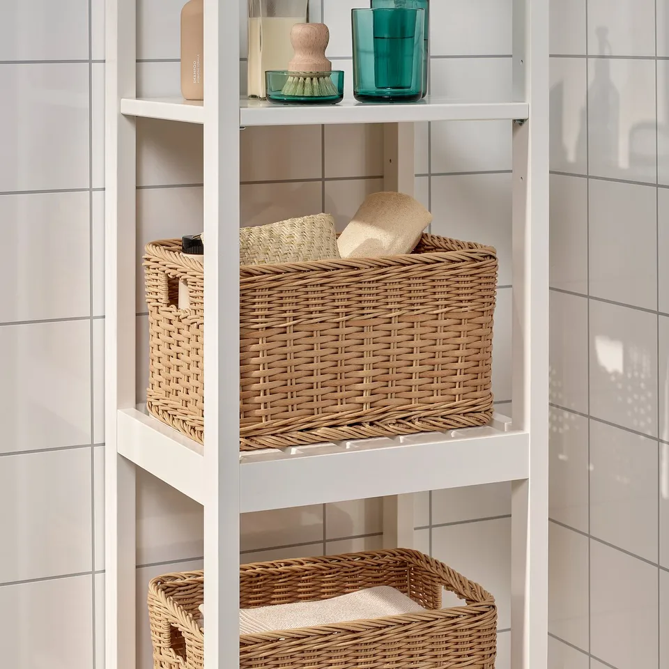 White bathroom shelf with wicker baskets for storage. Upper shelf has skincare items, lower shelves hold woven baskets for organising toiletries.