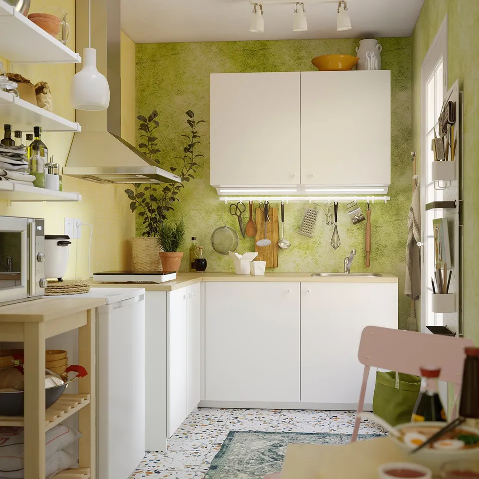 Bright kitchen with white KNOXHULT cabinets. Small, green-walled corner setup with portable hob, open shelves, and hanging utensils. 5-year guarantee.