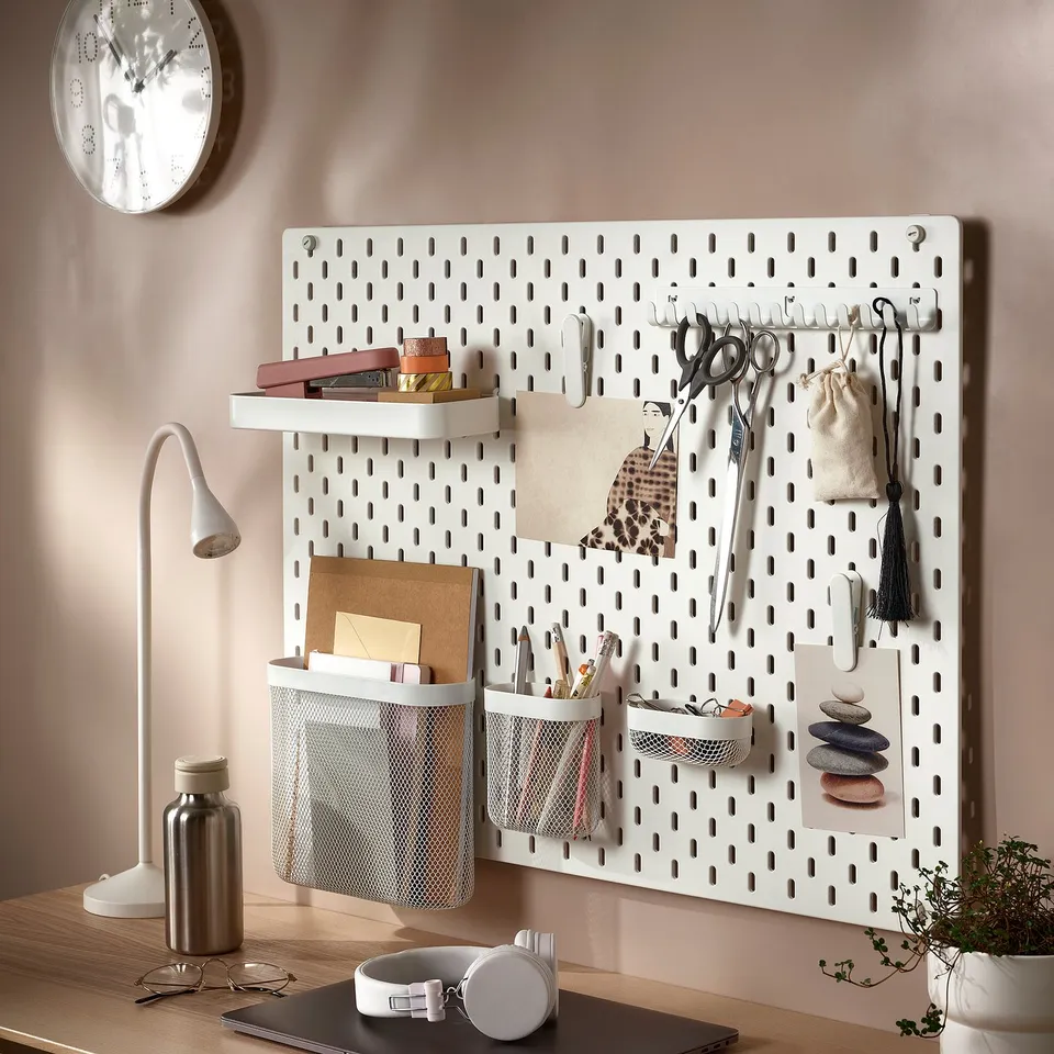 A white pegboard organises office supplies like scissors and pens with a lamp and clock nearby.