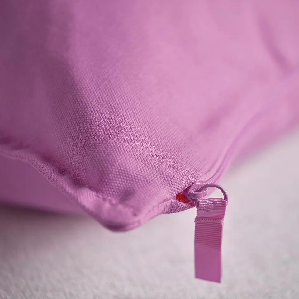 Close-up of a soft, pastel pink cushion with a zip and tag, showcasing its quality material and craftsmanship.