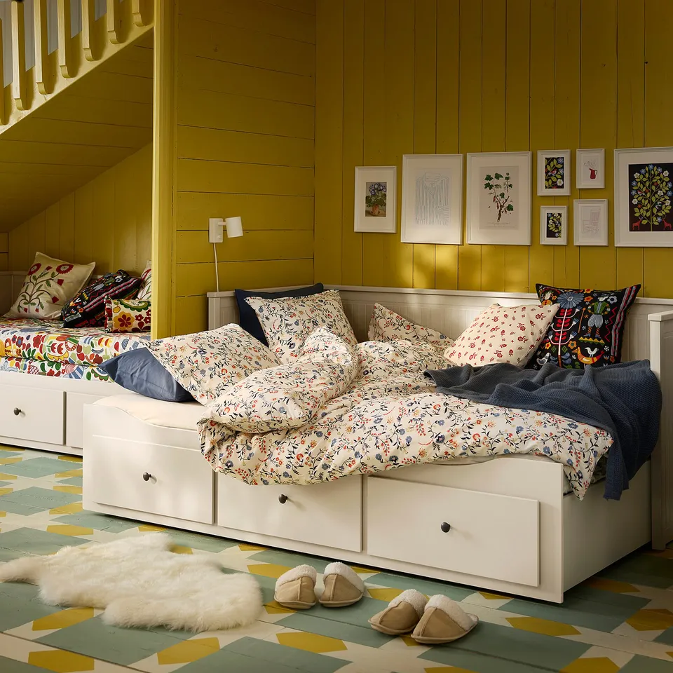 BRUDKRUSBÄR duvet on large bed with floral pattern, colourful pillows, green wall art, geometric rug, and slippers nearby.