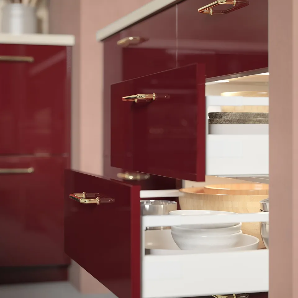 Modern kitchen with red cabinets, gold handles, and an open white drawer revealing white bowls. Small led lights are installed above the drawer.