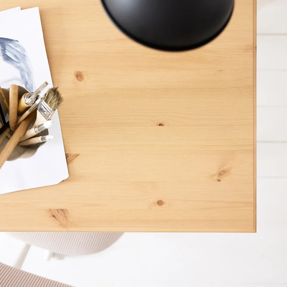 Wooden desk with artist supplies, brushes, and papers; shown from above.