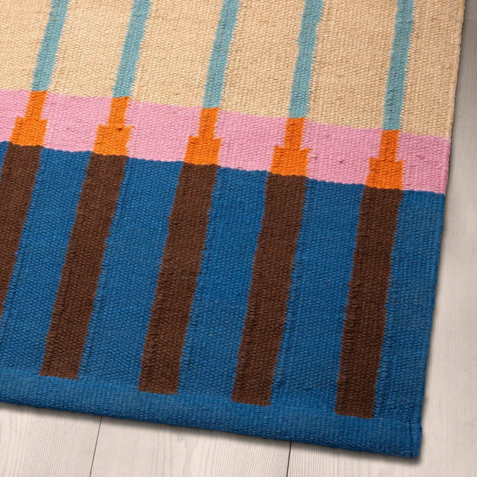 Brightly striped woven rug on wood floor. Blue, orange, pink, and beige stripes on jute base.