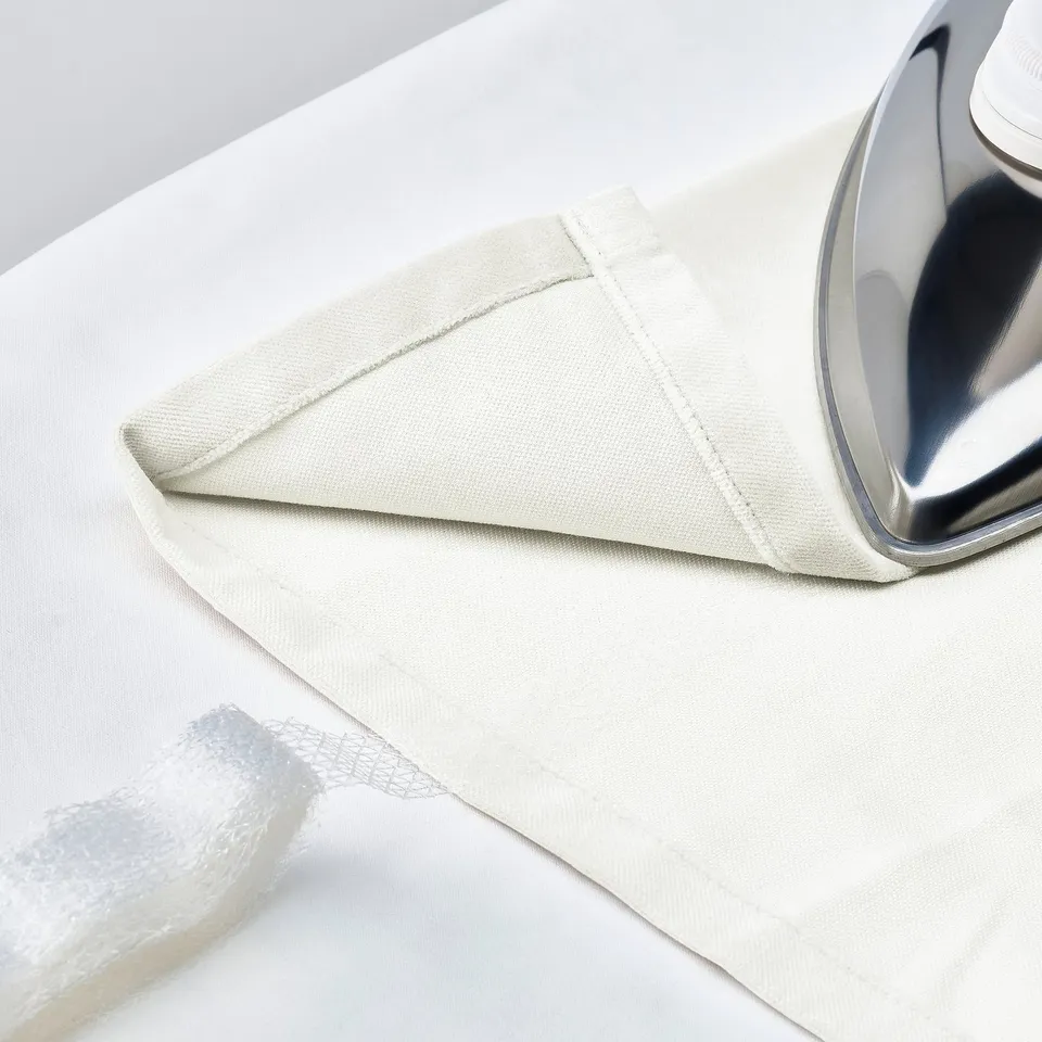 An iron near a folded beige curtain, with packaging beneath.