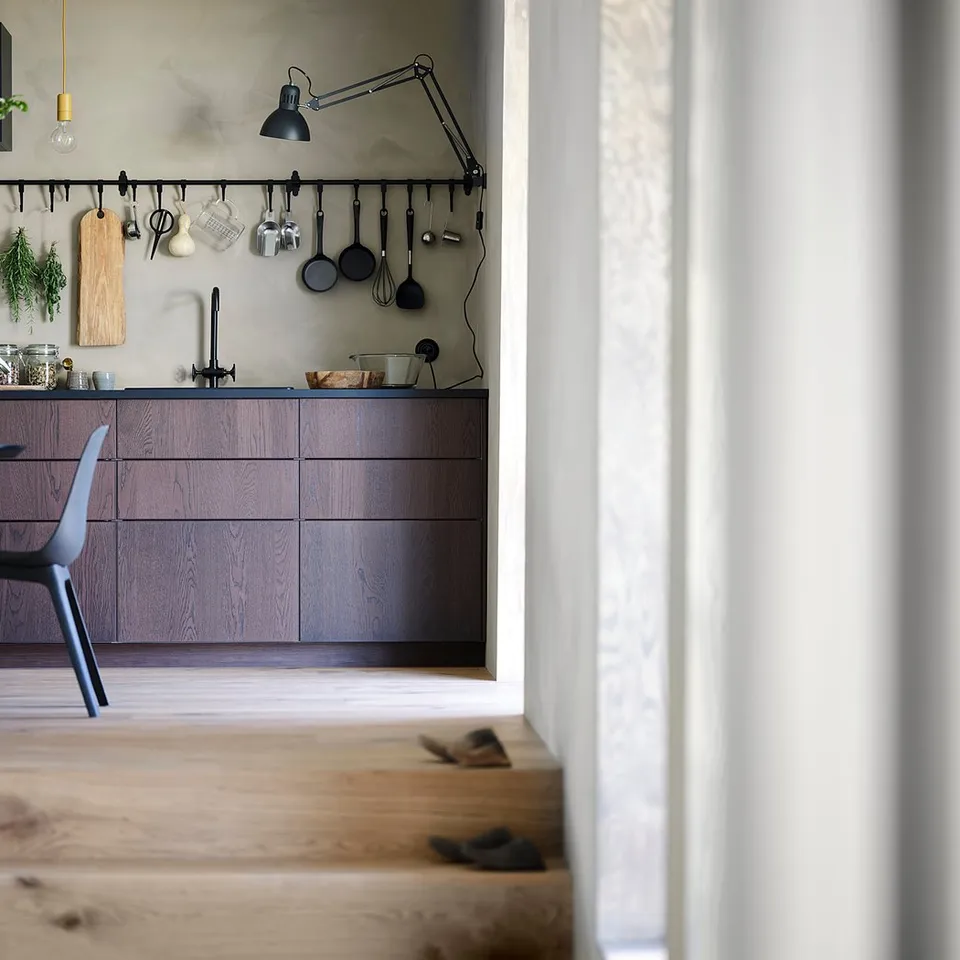 Modern kitchen with dark brown wooden cabinets and countertop, hanging utensils, and black chairs around a circular table.