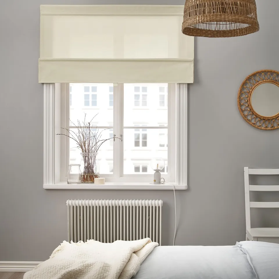 Minimalist bedroom with large bed, filtered daylight blinds, wicker mirror.