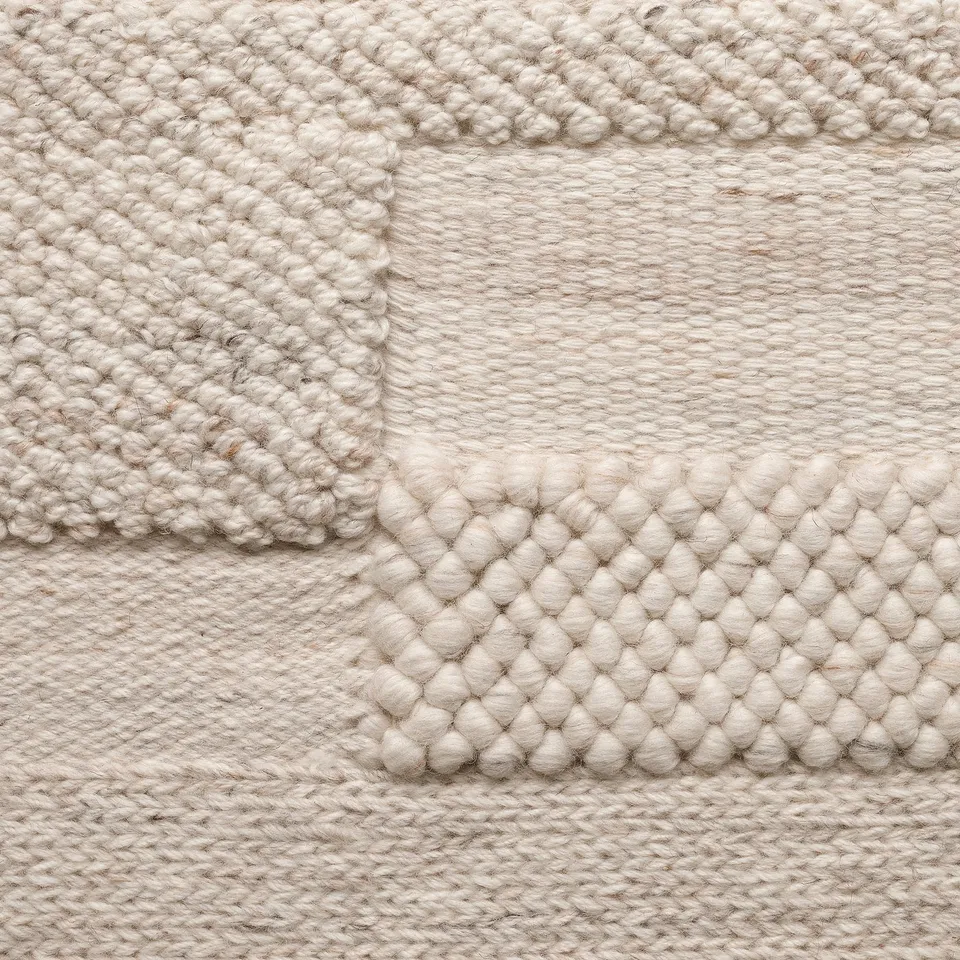 Handwoven wool rug, neutral tone, varied textures, intricate patterns.