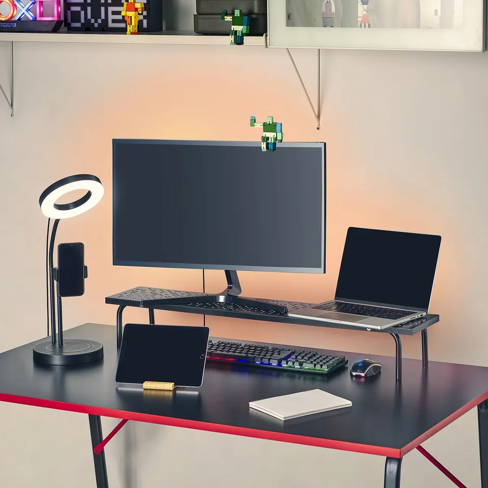 Desk setup with monitor stand, keyboard, laptop, tablet, mouse, and ring lamp.