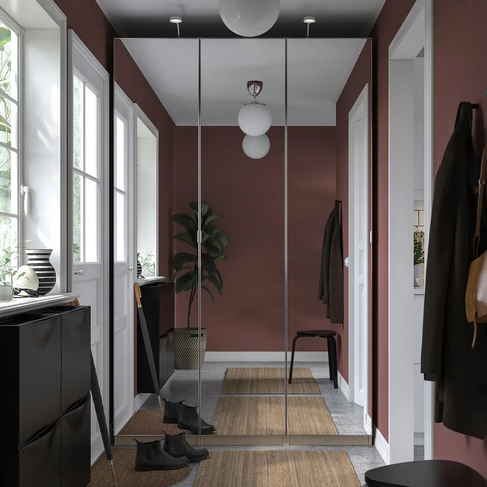 Modern closet with red walls, mirrored doors, hanging coats, and black boots.