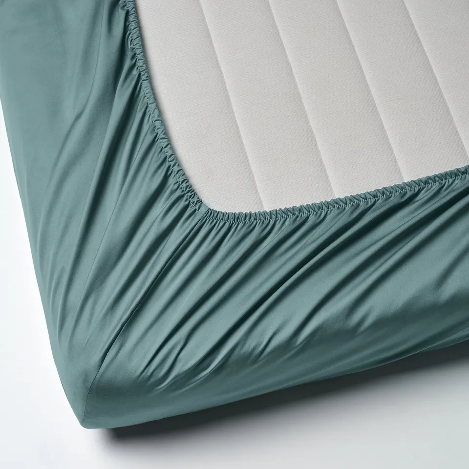 Corner of smooth, teal bed sheet on white mattress. Elastic hem, smooth sateen weave.
