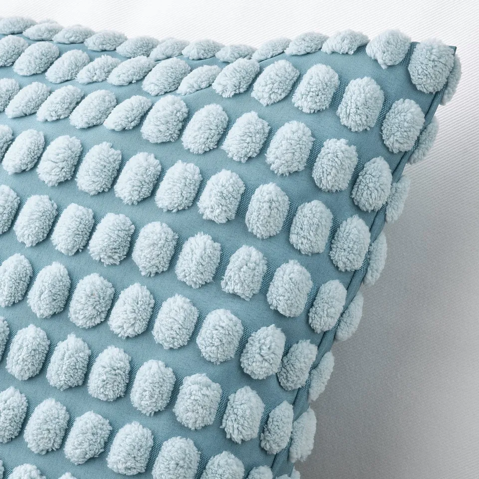 Decorative light blue pillow with soft, white, pom-pom-like accents, neatly arranged in rows, against a white background.