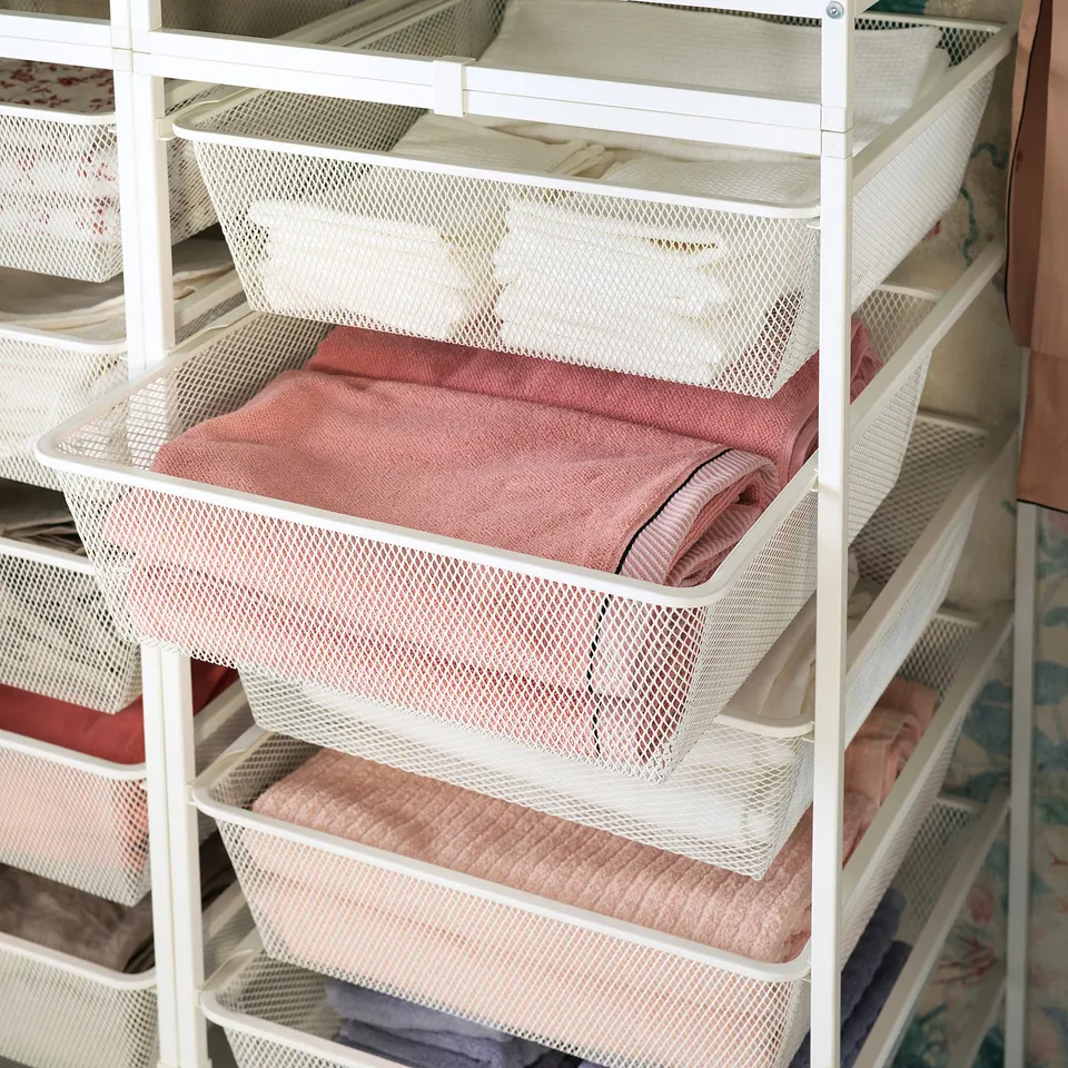 White JONAXEL storage shelves with mesh baskets, pink towels organised, durable metal design.