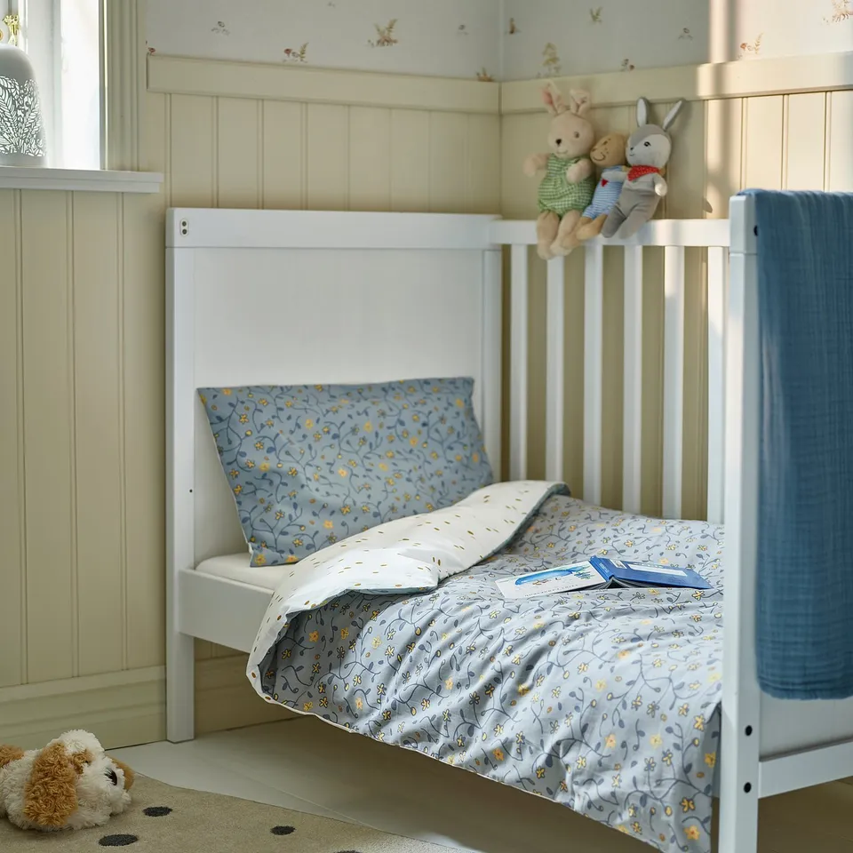 GULDVÄVARE: blue floral baby duvet set. White frame bed, soft toys. Fits perfectly in cosy room setting.