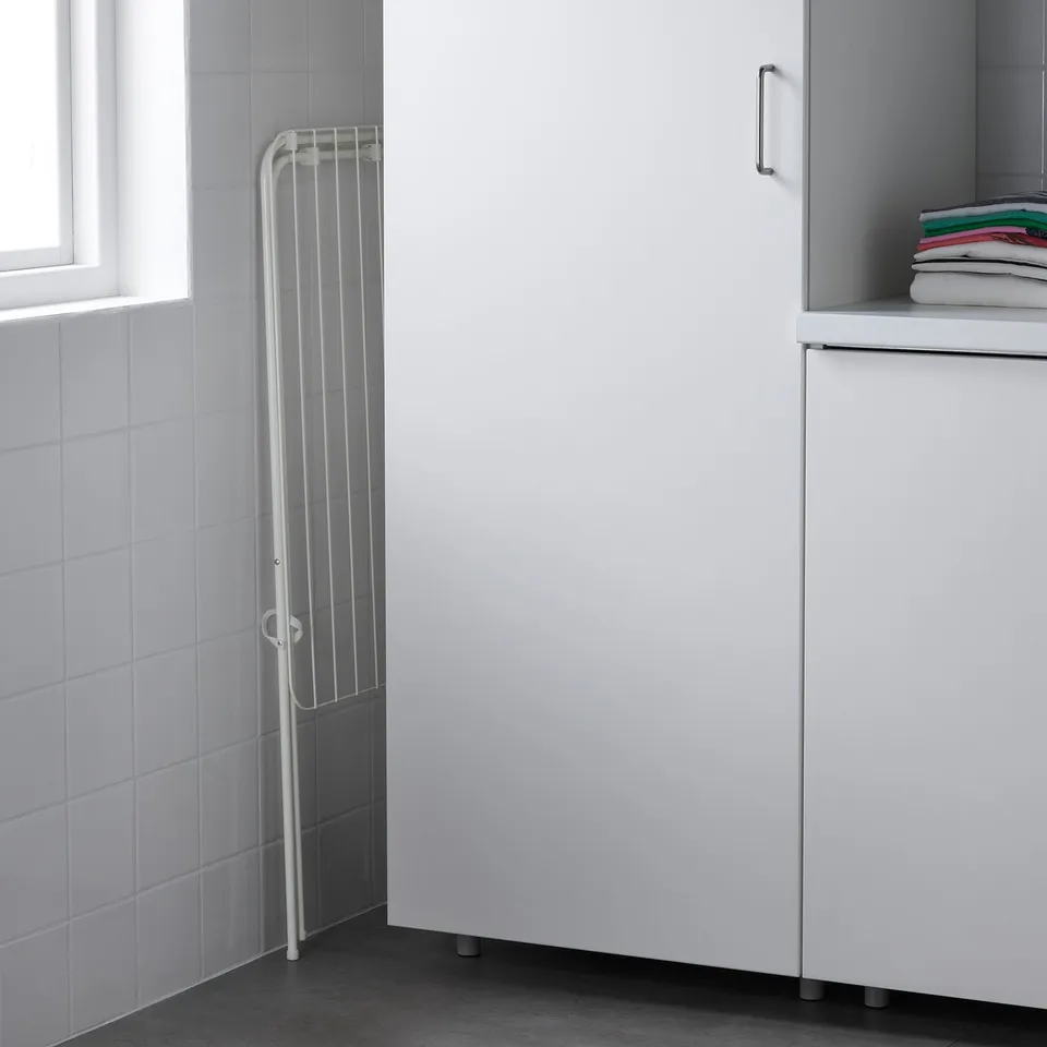 White clothes drying rack between tiled walls and a cabinet with folded towels, slim and space-efficient.