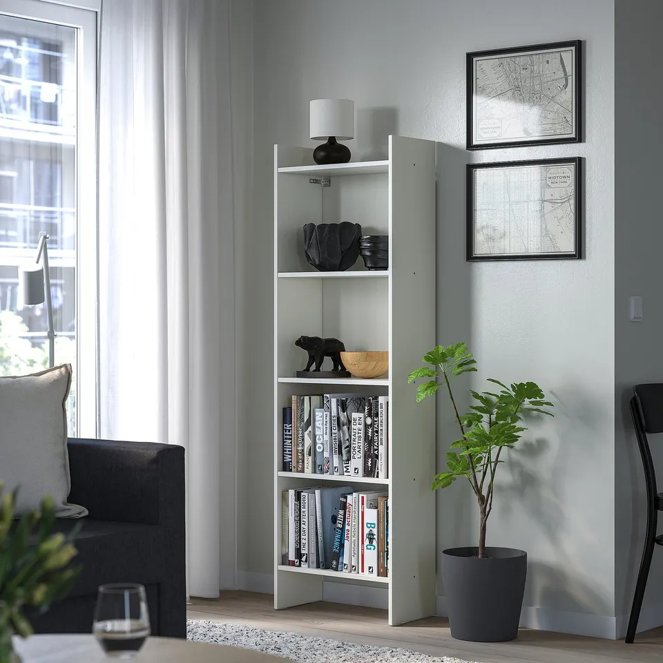 Modern living room with BAGGEBO bookcase, books, decor, grey walls, large windows, dark sofa, plants.